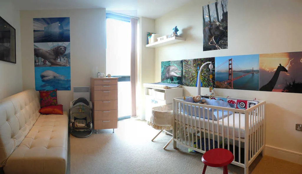 Babykamer met wanddecoratie van kleurrijke posters boven een witte wieg en commode