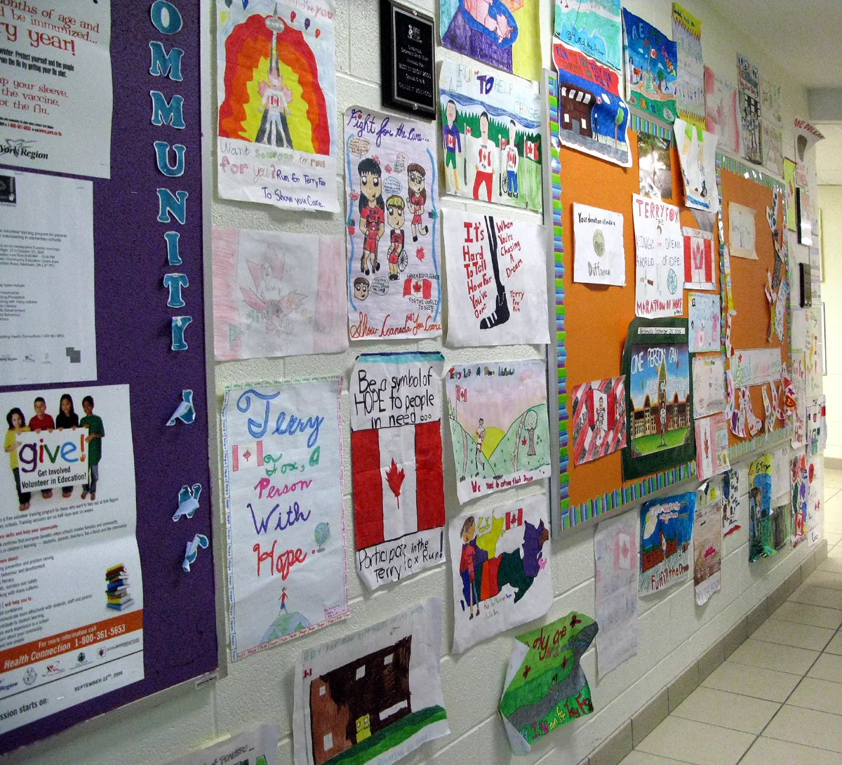 Muur met een groot aantal kindertekeningen en posters op prikborden in een schoolgang